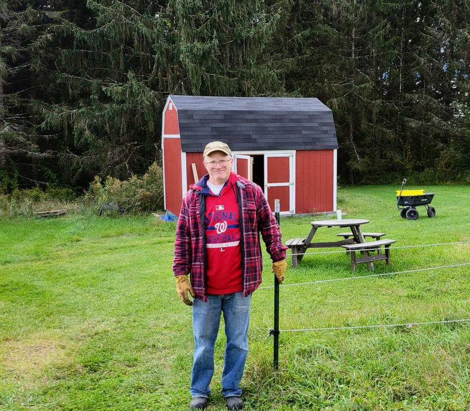 Farmer standing in front of a picnic table and red barn